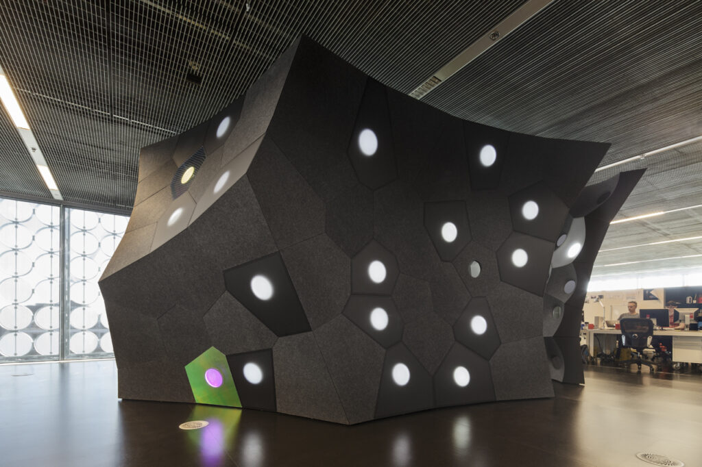 A black pavilion with concave facets sits in a room for exhibition